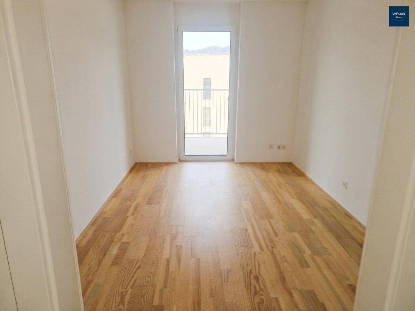 Leerer Raum mit hellem Holzboden und Zugang zu einem französischen Balkon, ideal für Schlaf- oder Wohnzimmer.