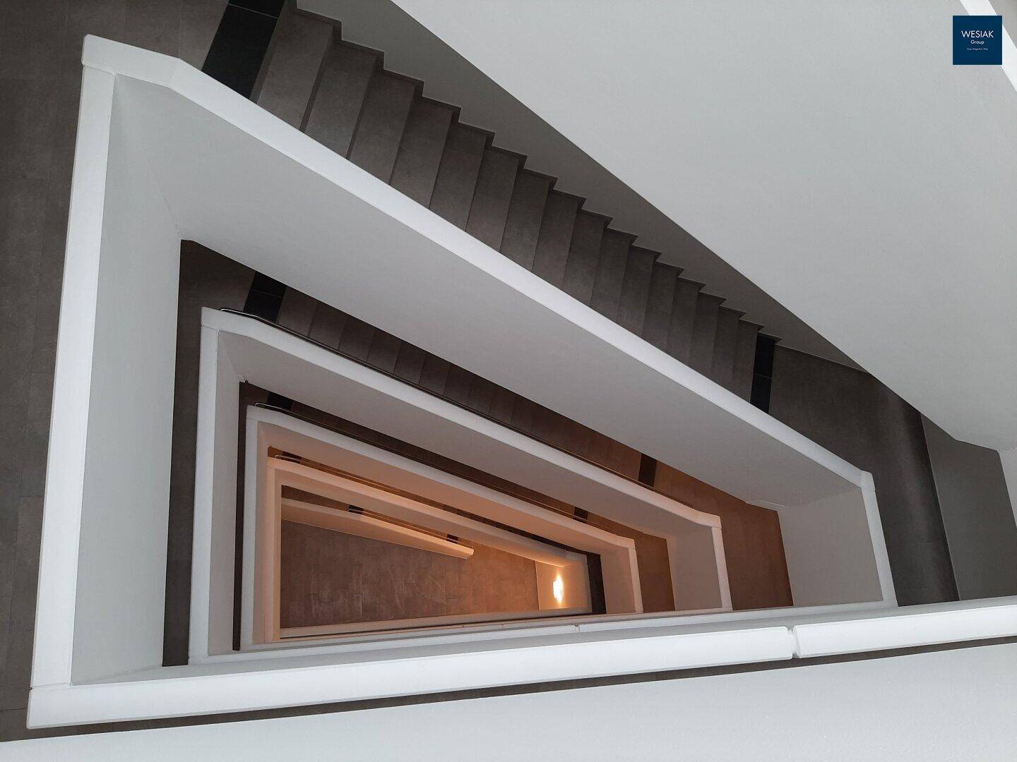 Modernes Treppenhaus mit klaren Linien und minimalistischem Design, von oben nach unten fotografiert.