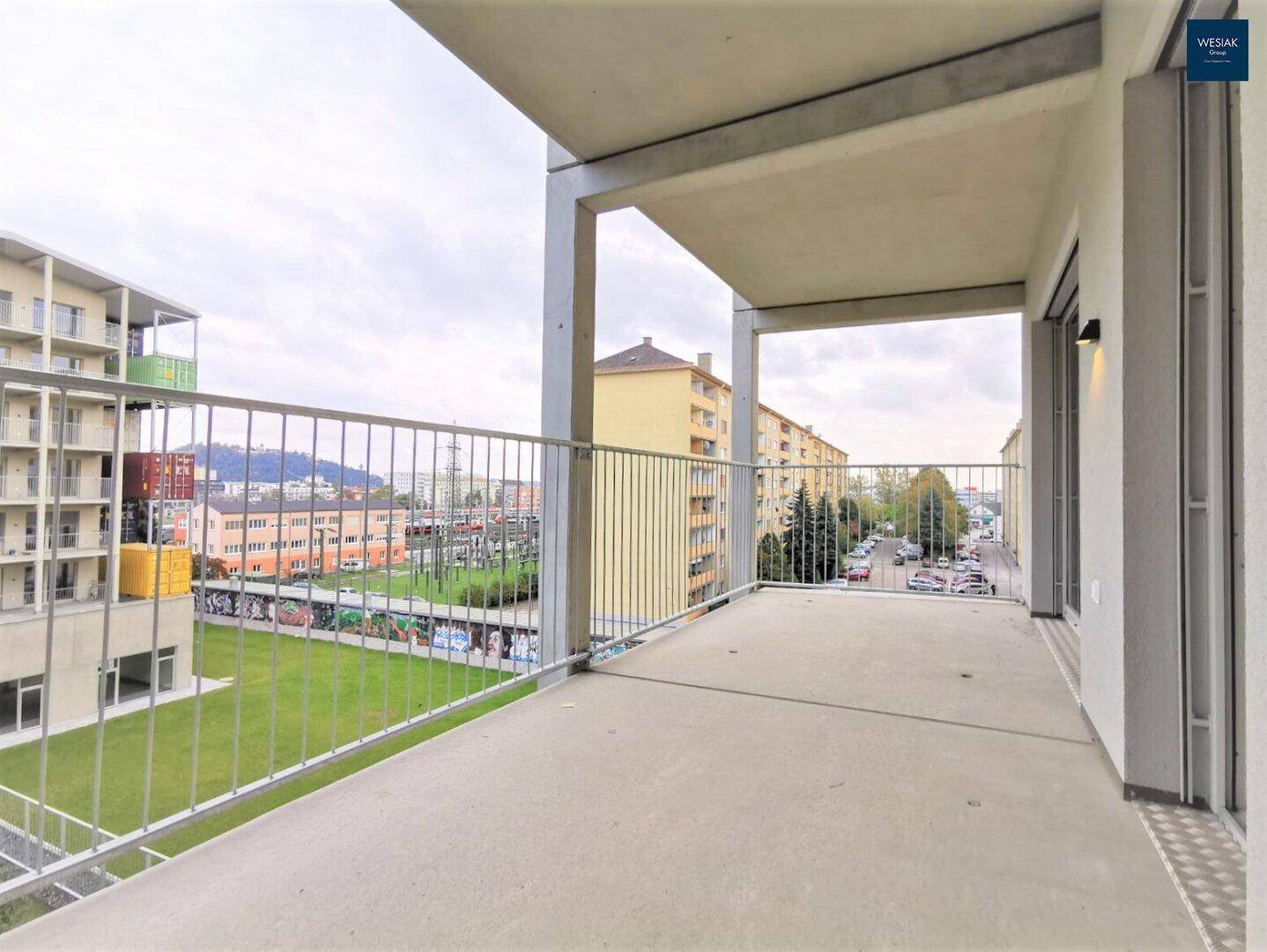 Geräumiger Balkon mit Metallgeländer und Blick auf die umliegende Stadt und Gebäude.