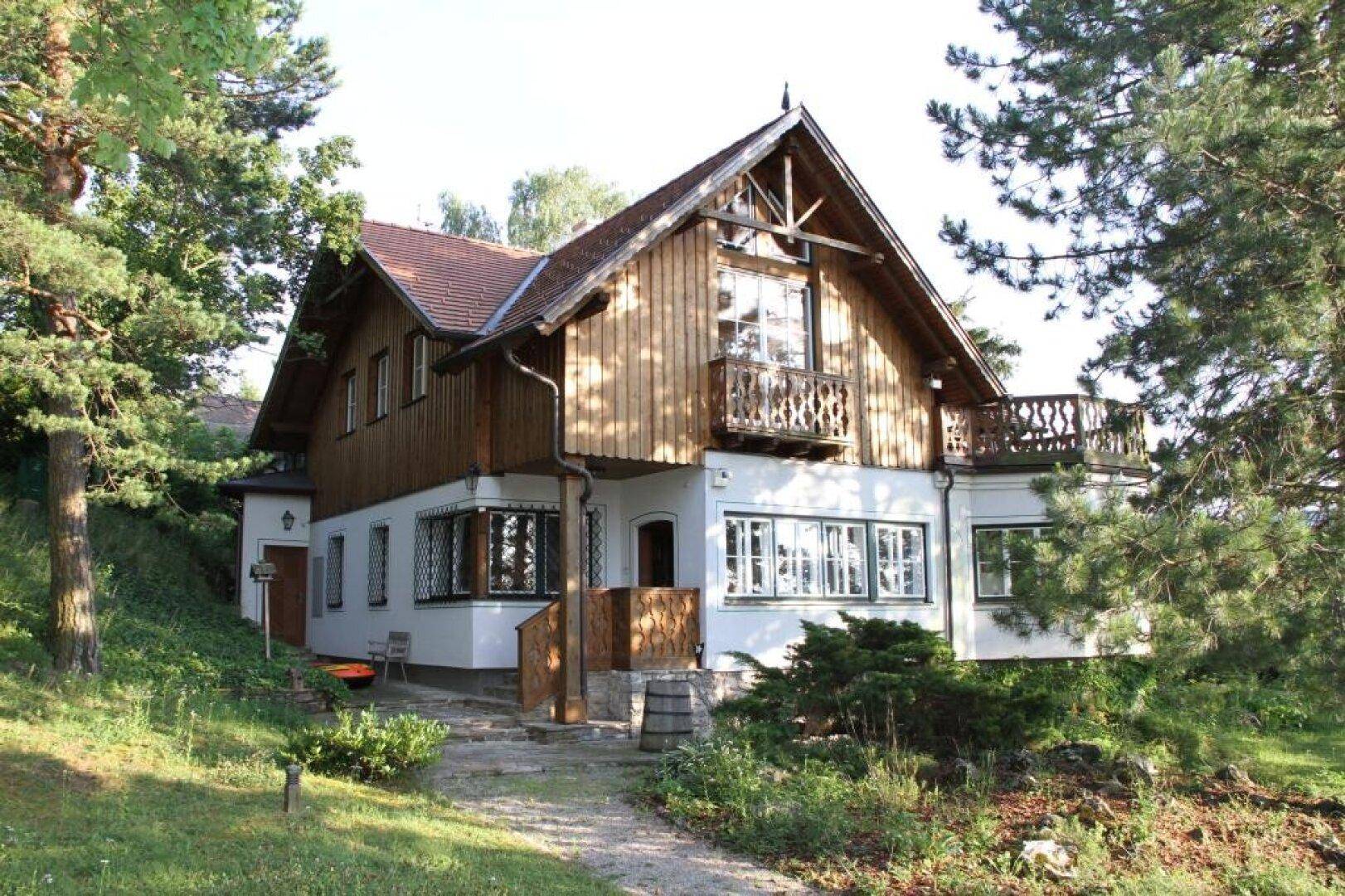 Traditionelles Haus mit Holzfassade, weißen Wänden und mehreren Balkonen im Grünen.