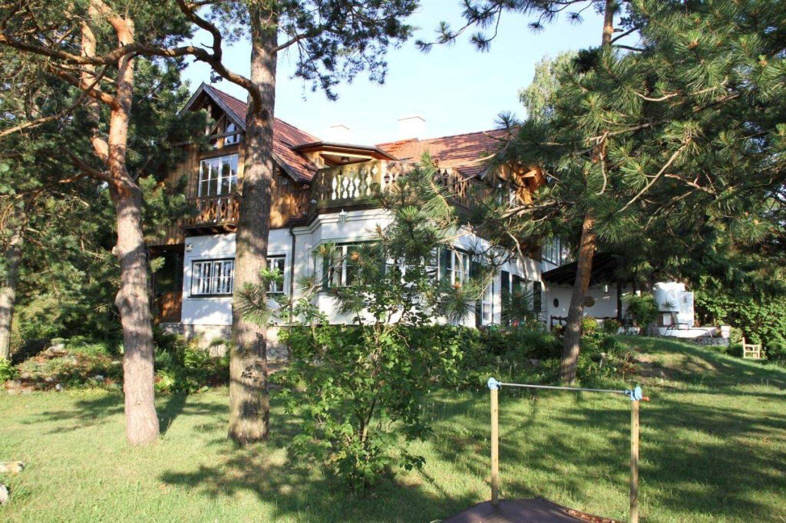 Vorderansicht des Hauses mit großem Garten und Spielgeräten, umgeben von Bäumen.