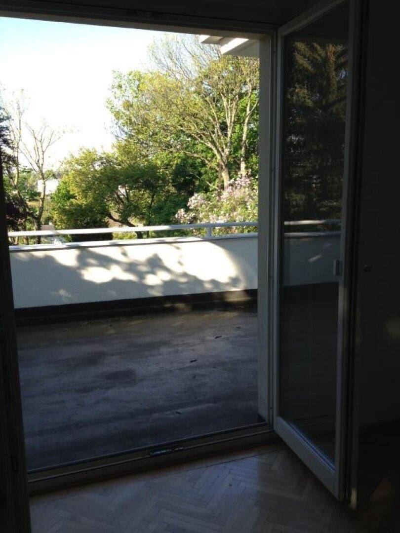 Blick von einem Innenraum auf einen Balkon oder eine Terrasse mit grüner Aussicht.