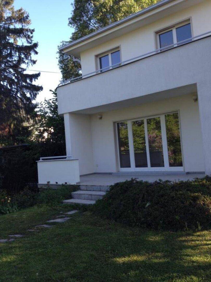 Moderne weiße Hausfassade mit großen Fenstern und einem kleinen Eingangsbereich.
