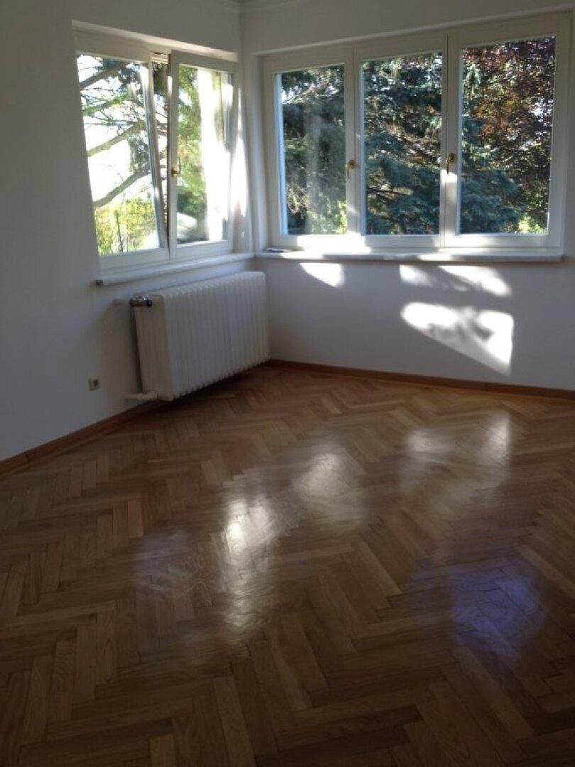 Heller Raum mit Fischgrätparkett, weißen Wänden und großen Fenstern, die viel Licht hereinlassen.