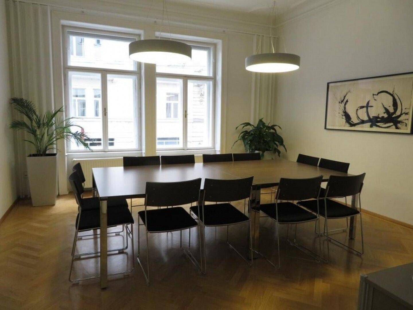 Geräumiger Konferenzraum mit großem Holztisch, modernen Pendelleuchten und Fischgrätparkett.
