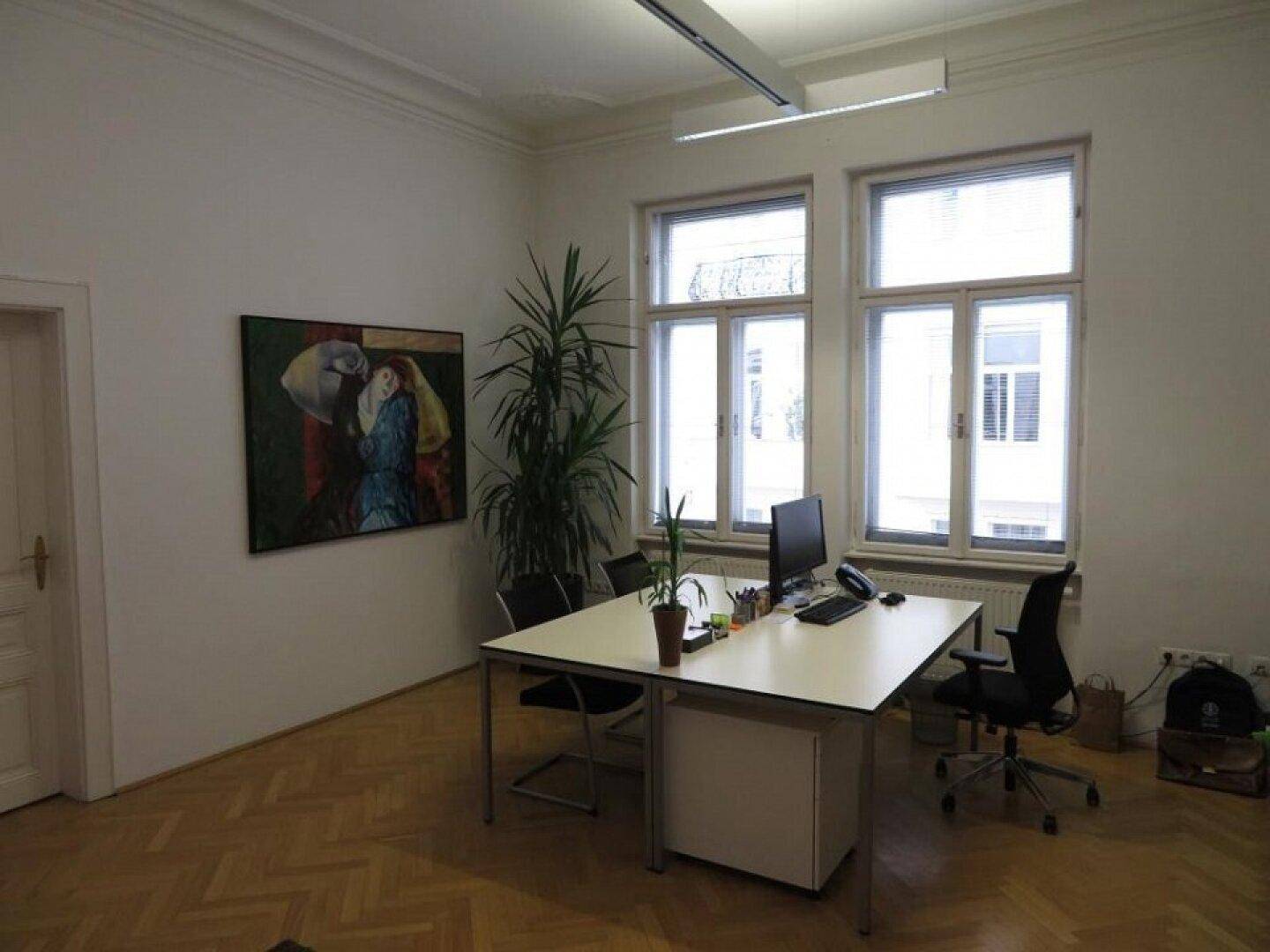 Helles Büro mit Schreibtisch, Computer und Pflanzen, ausgestattet mit Fischgrätparkett und großen Fenstern.