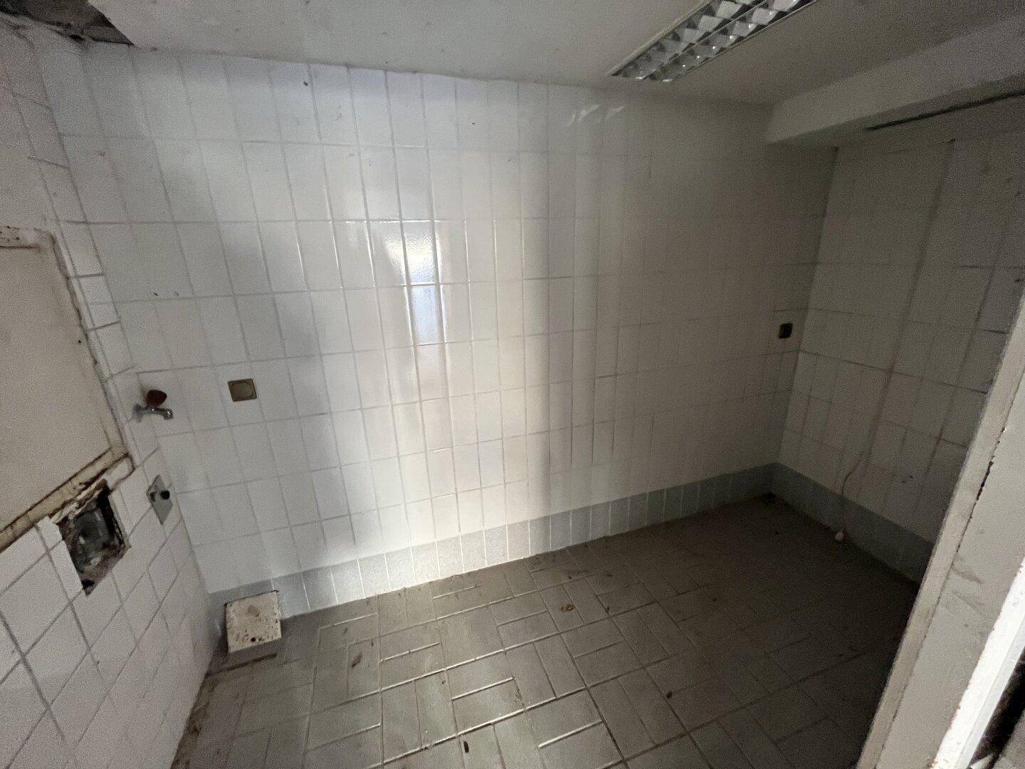 Kleiner, gefliester Hauswirtschaftsraum mit Wasseranschluss und einfacher Beleuchtung, zeigt Gebrauchsspuren.