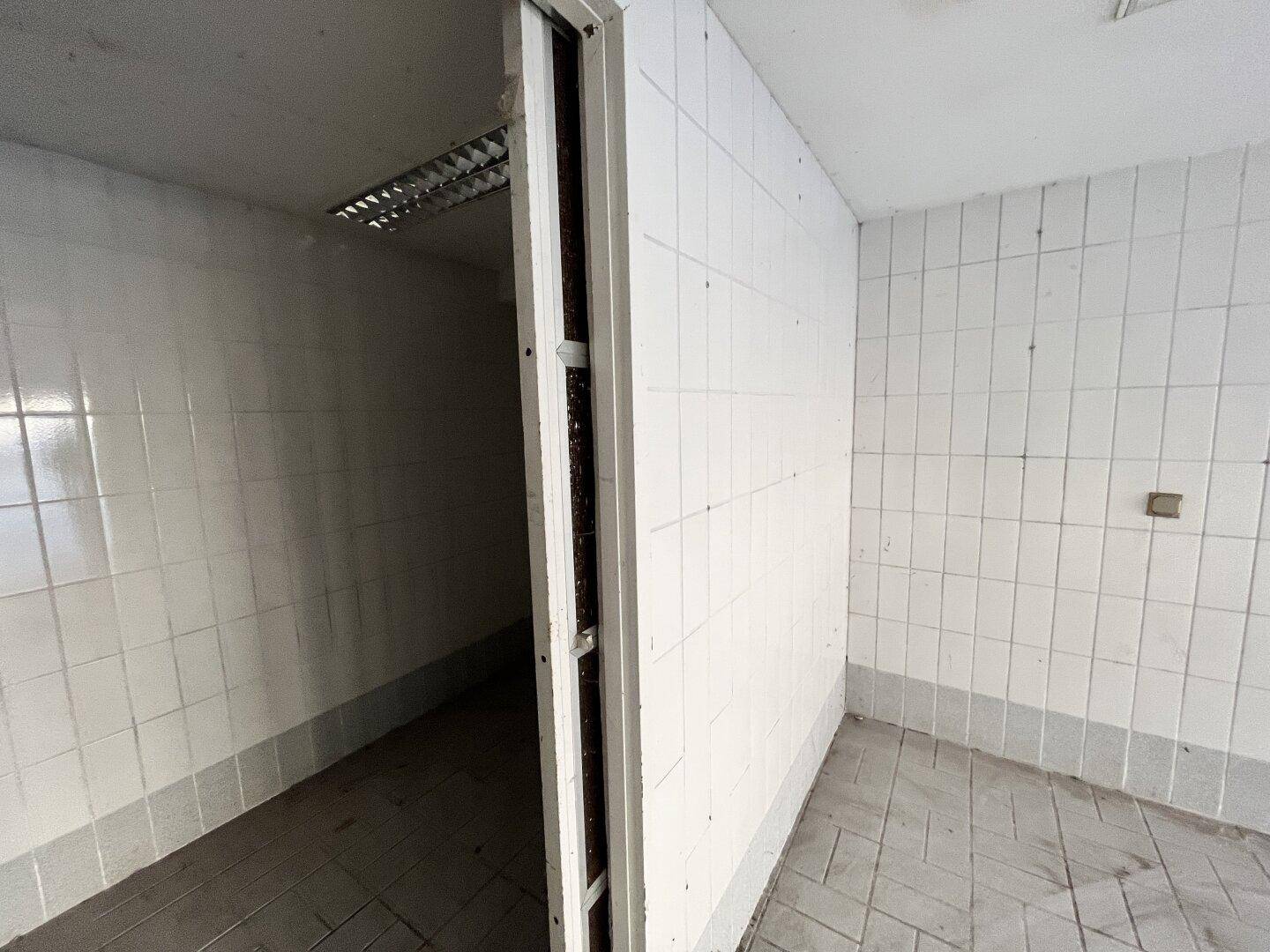 Gefliester Flur oder Durchgangsbereich mit weißen Wandfliesen und einfacher Deckenbeleuchtung.