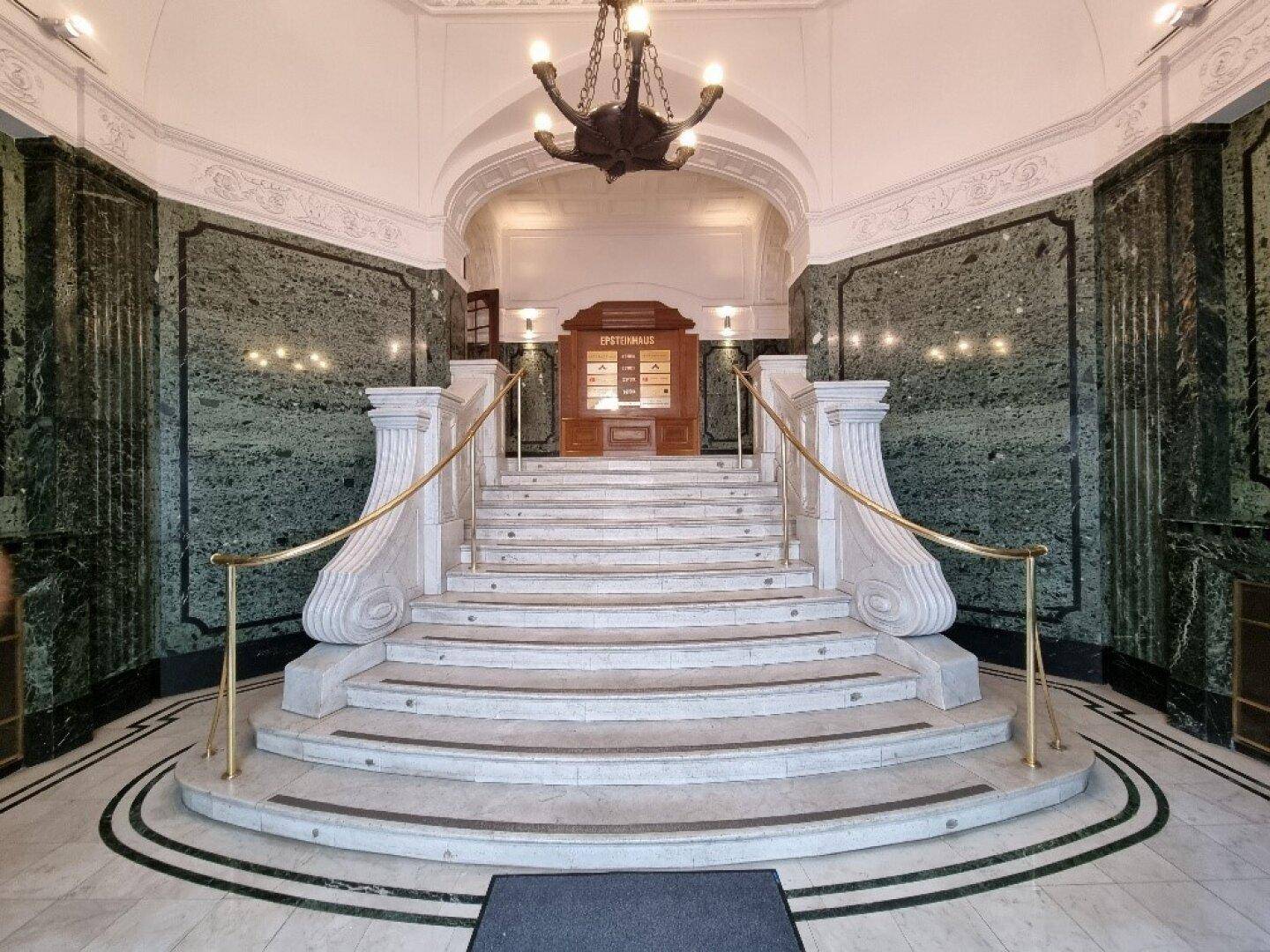 Elegante Eingangshalle mit einer geschwungenen Marmortreppe, grünen Marmorverkleidungen und einem historischen Kronleuchter.