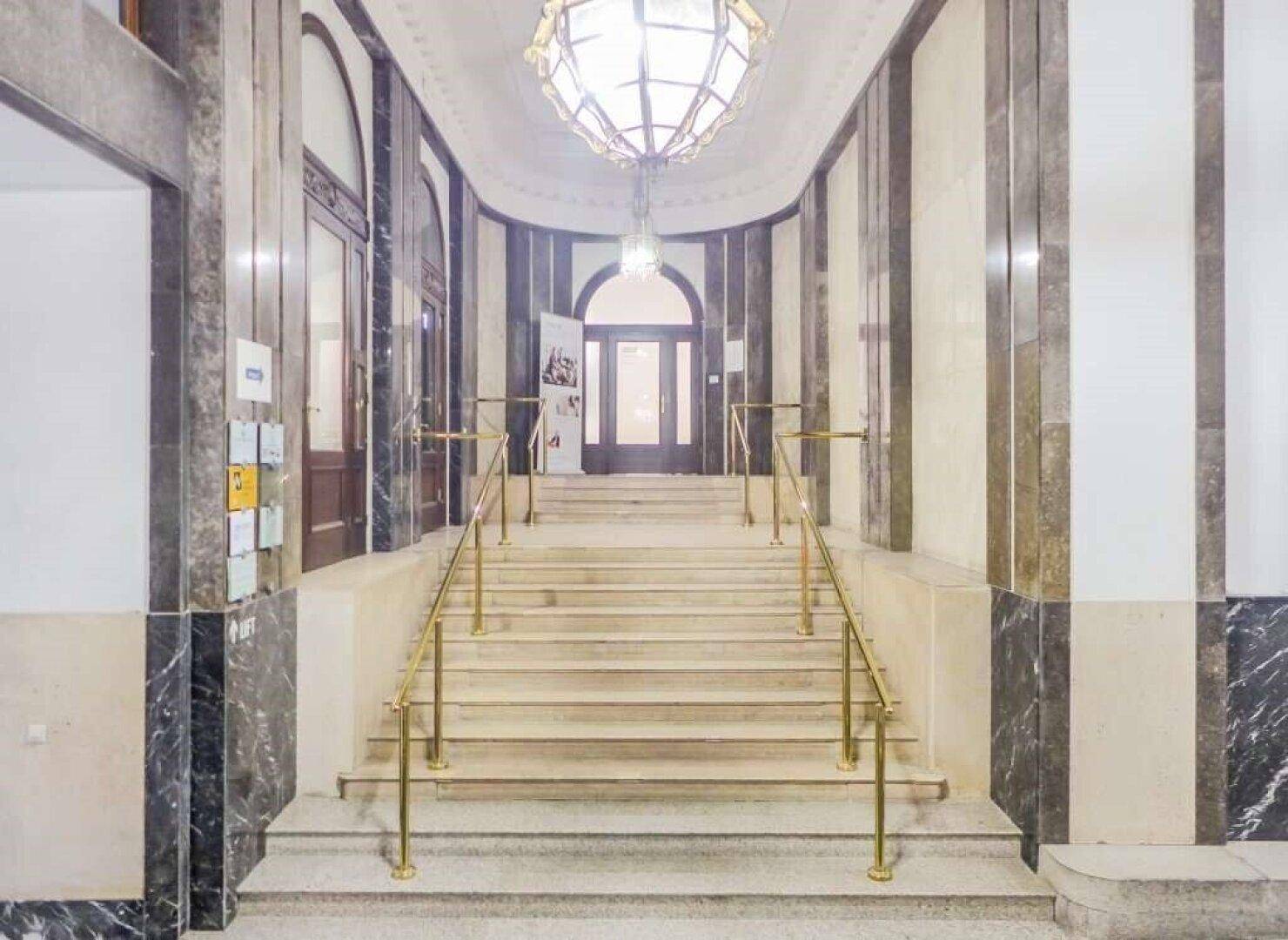 Elegantes Treppenhaus mit Marmorstufen, goldenen Handläufen und einer dekorativen Deckenleuchte.