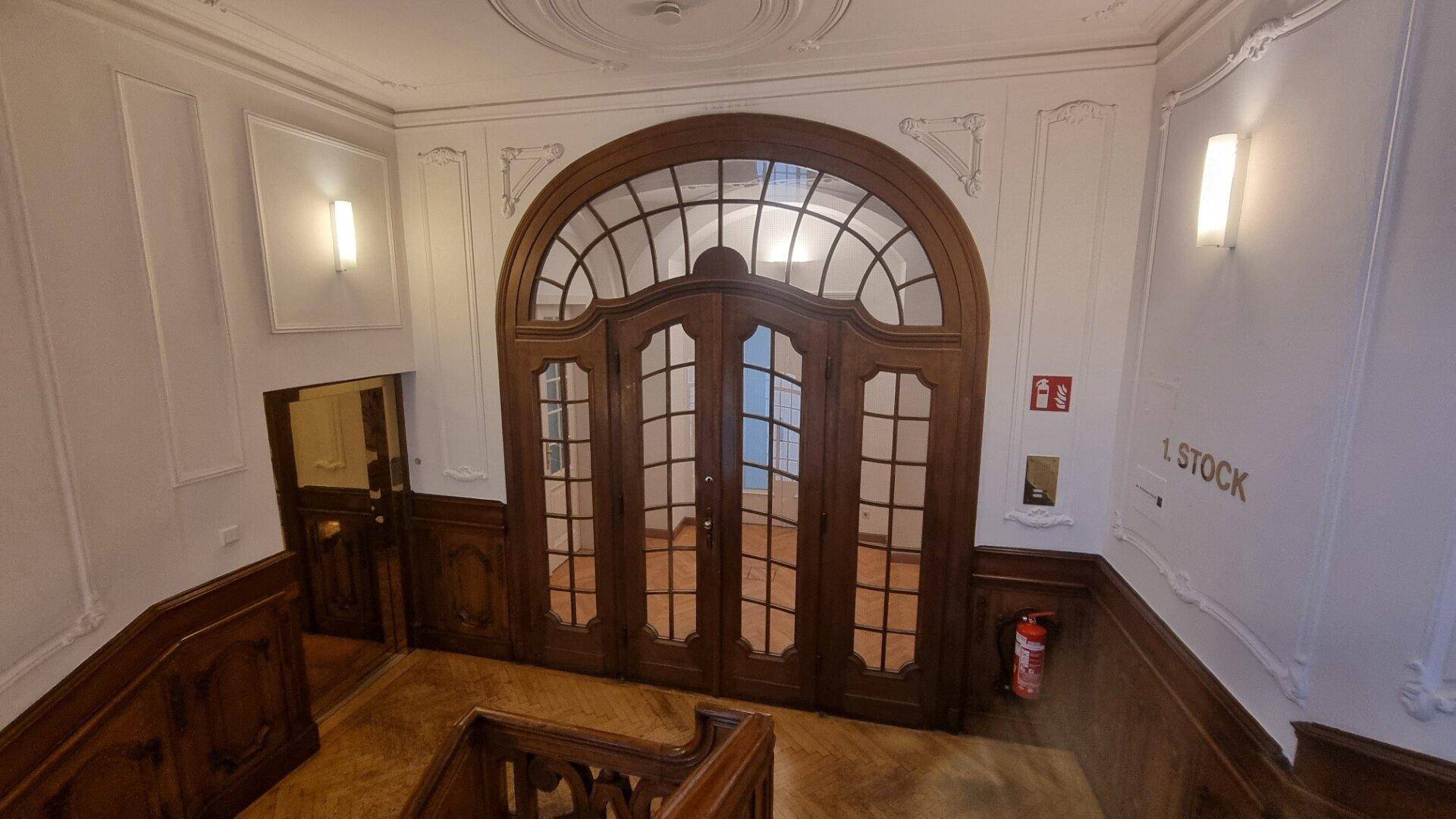 Eindrucksvoller Treppenaufgang mit einer großen, verzierten Holztür und Stuckdecken in einem Altbau.