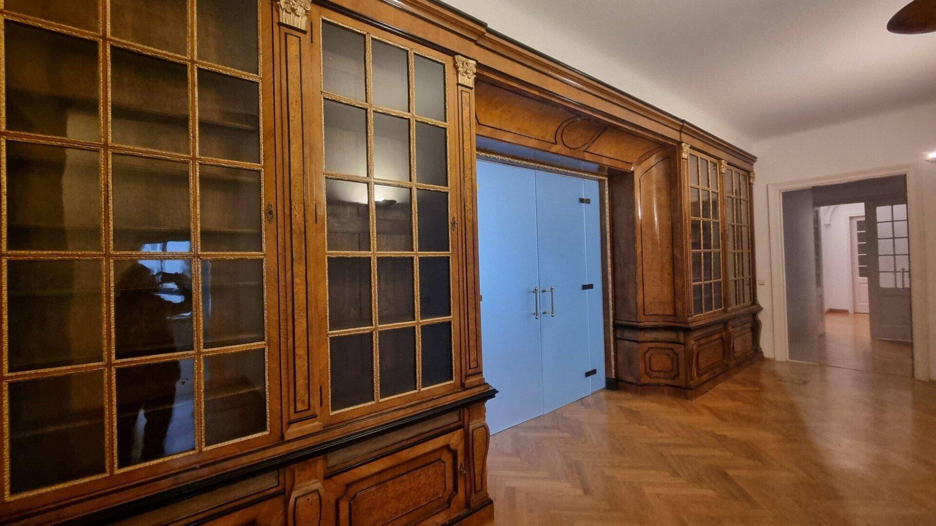 Elegante Einbauschränke aus Holz mit Glasfronten und Fischgrätparkett in einem Flur.