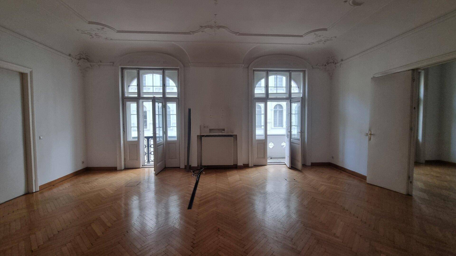 Geräumiges Zimmer mit Fischgrätparkett, Stuckdecke und zwei französischen Balkonen.