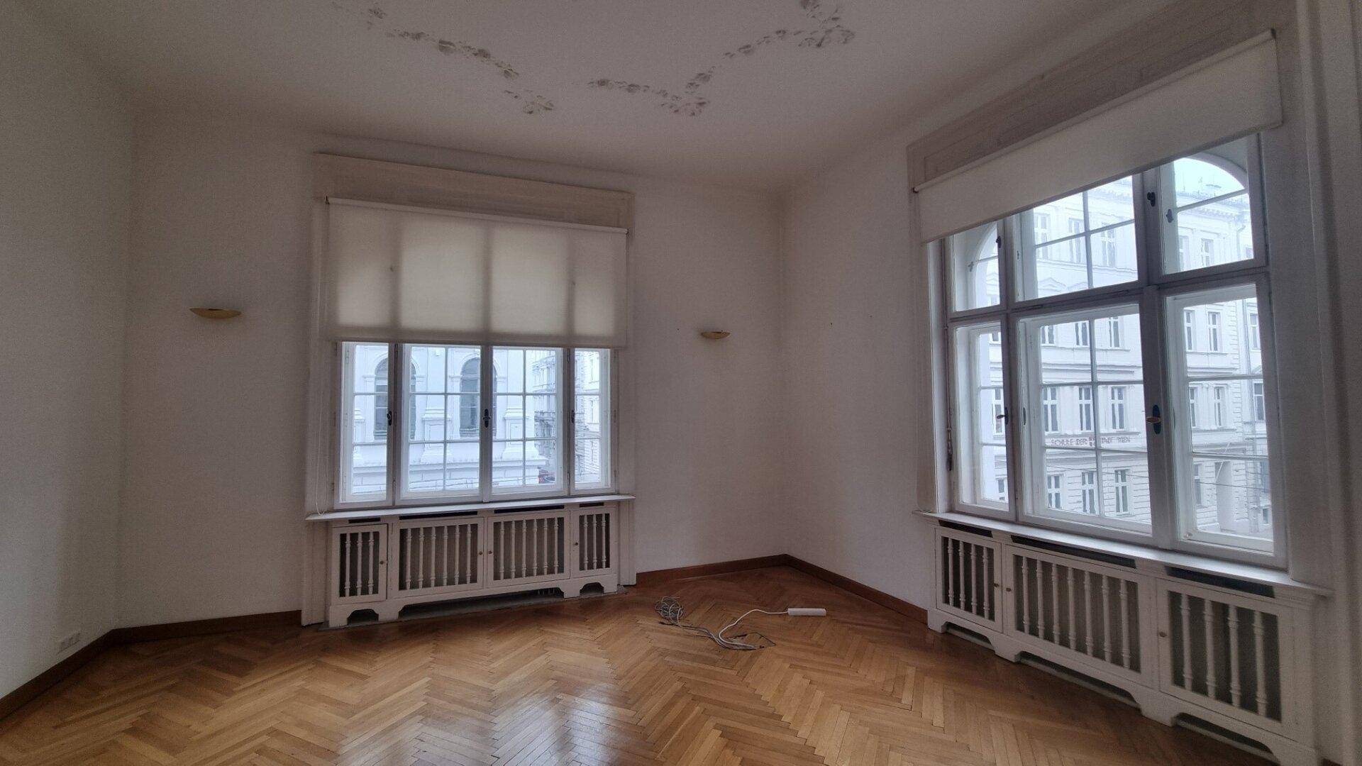 Helles Zimmer mit großen Fenstern, Fischgrätparkett und Stuckdecke, Blick auf die Straße.
