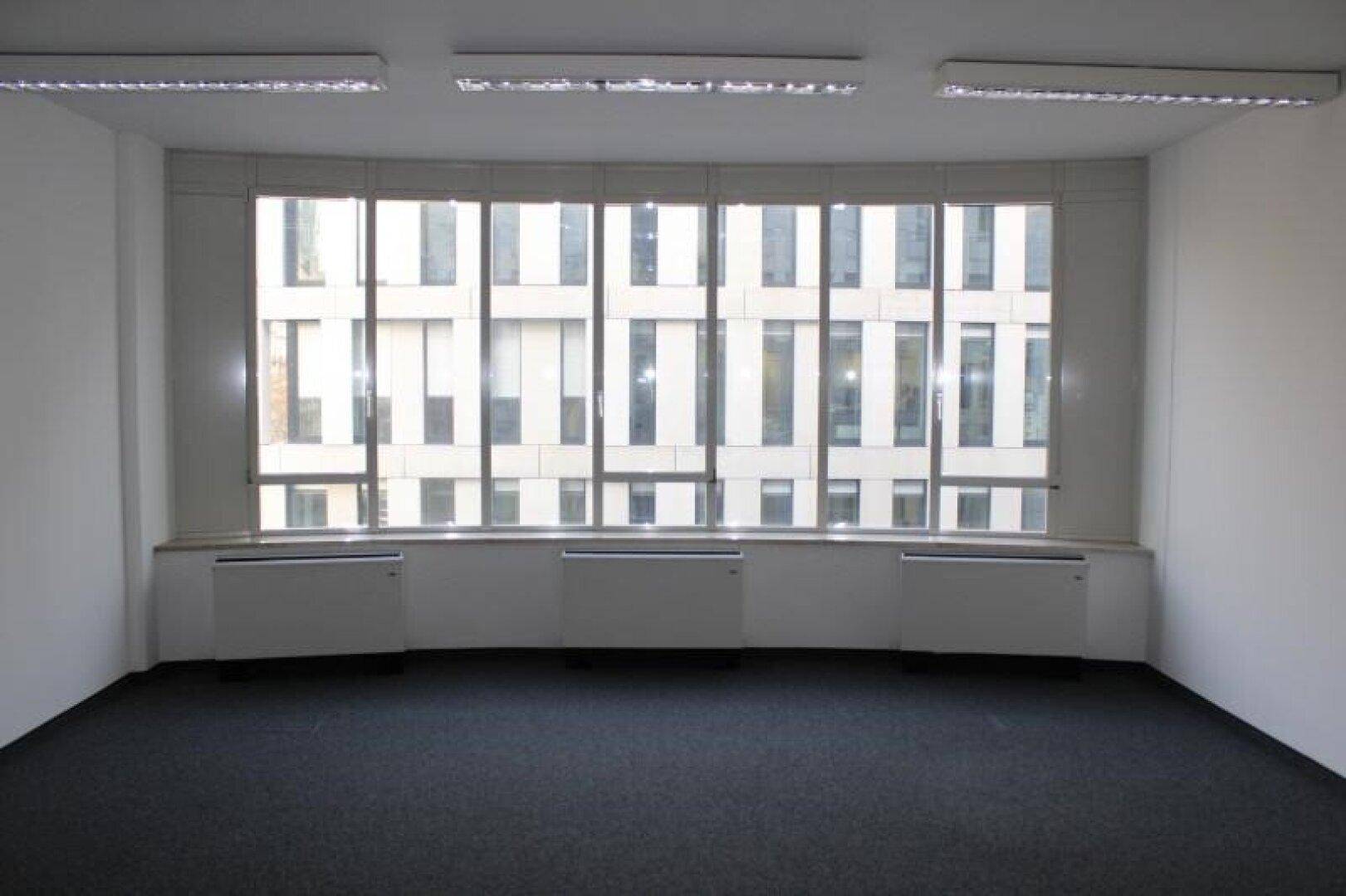 Geräumiger Büroraum mit einer breiten Fensterfront, die viel Tageslicht hereinlässt und einen urbanen Ausblick bietet.