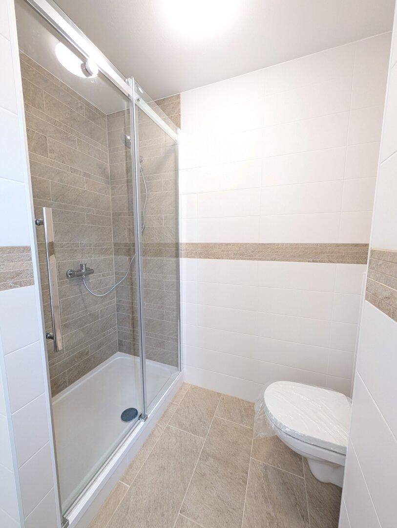 Modernes Badezimmer mit begehbarer Dusche, Glasabtrennung und wandhängendem WC.