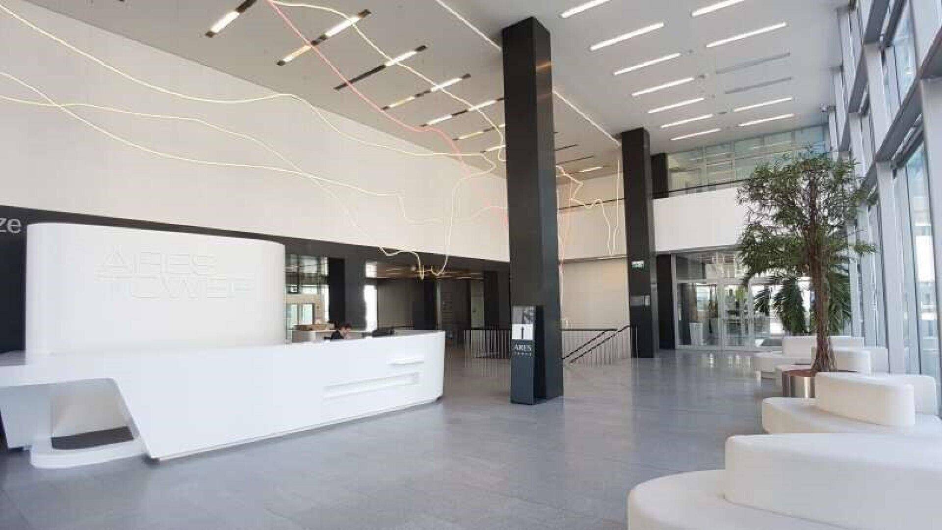 Geräumige und moderne Lobby mit weißer Rezeption, Sitzgelegenheiten und hohen Decken.