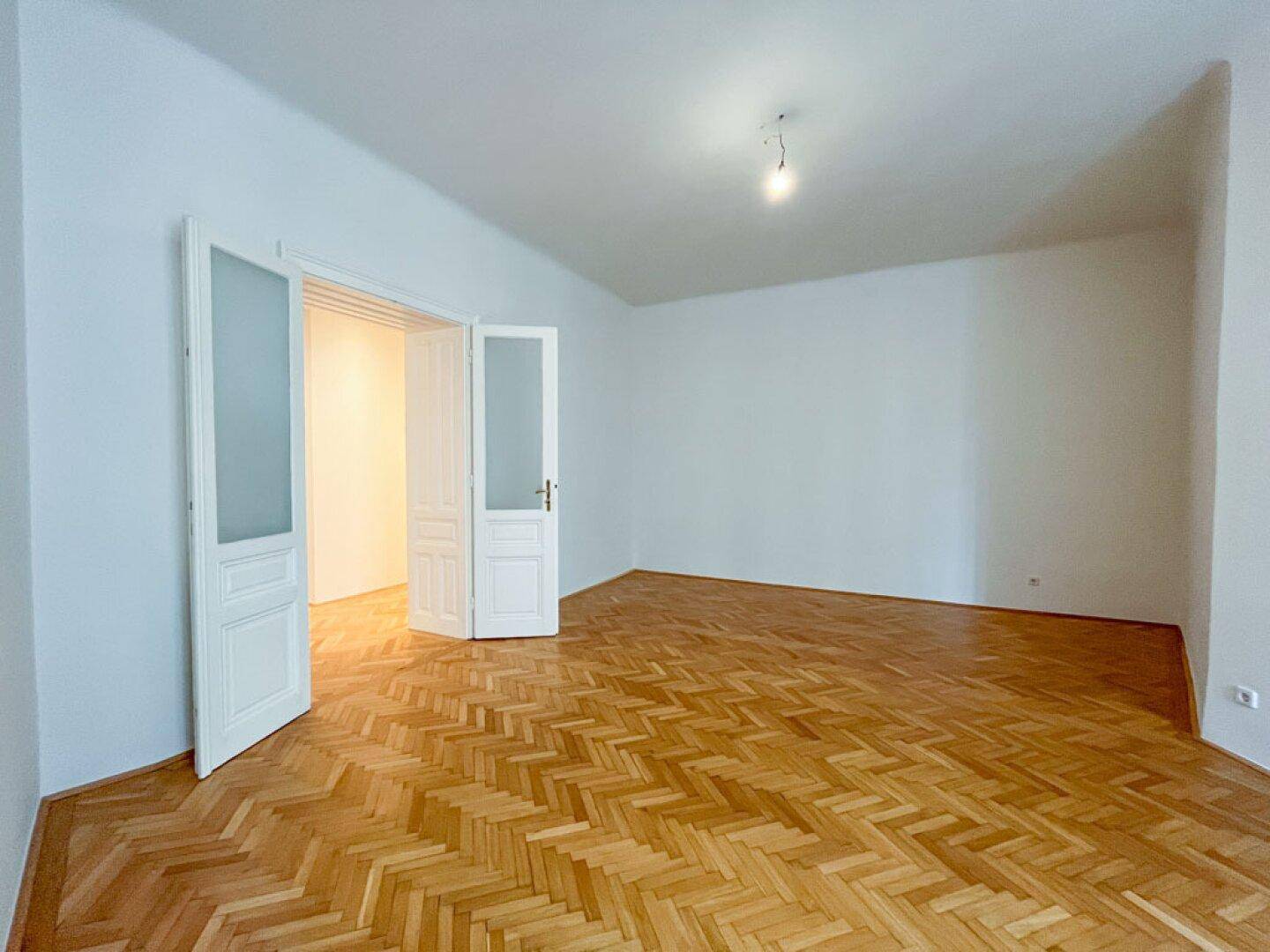 Geräumiges Zimmer mit Fischgrätparkett und eleganten Doppeltüren mit Milchglas, die Licht durchlassen.