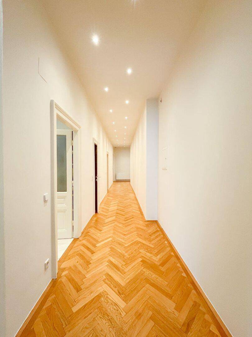 Langer, heller Flur mit klassischem Fischgrätparkett und modernen Einbaustrahlern in der Decke.