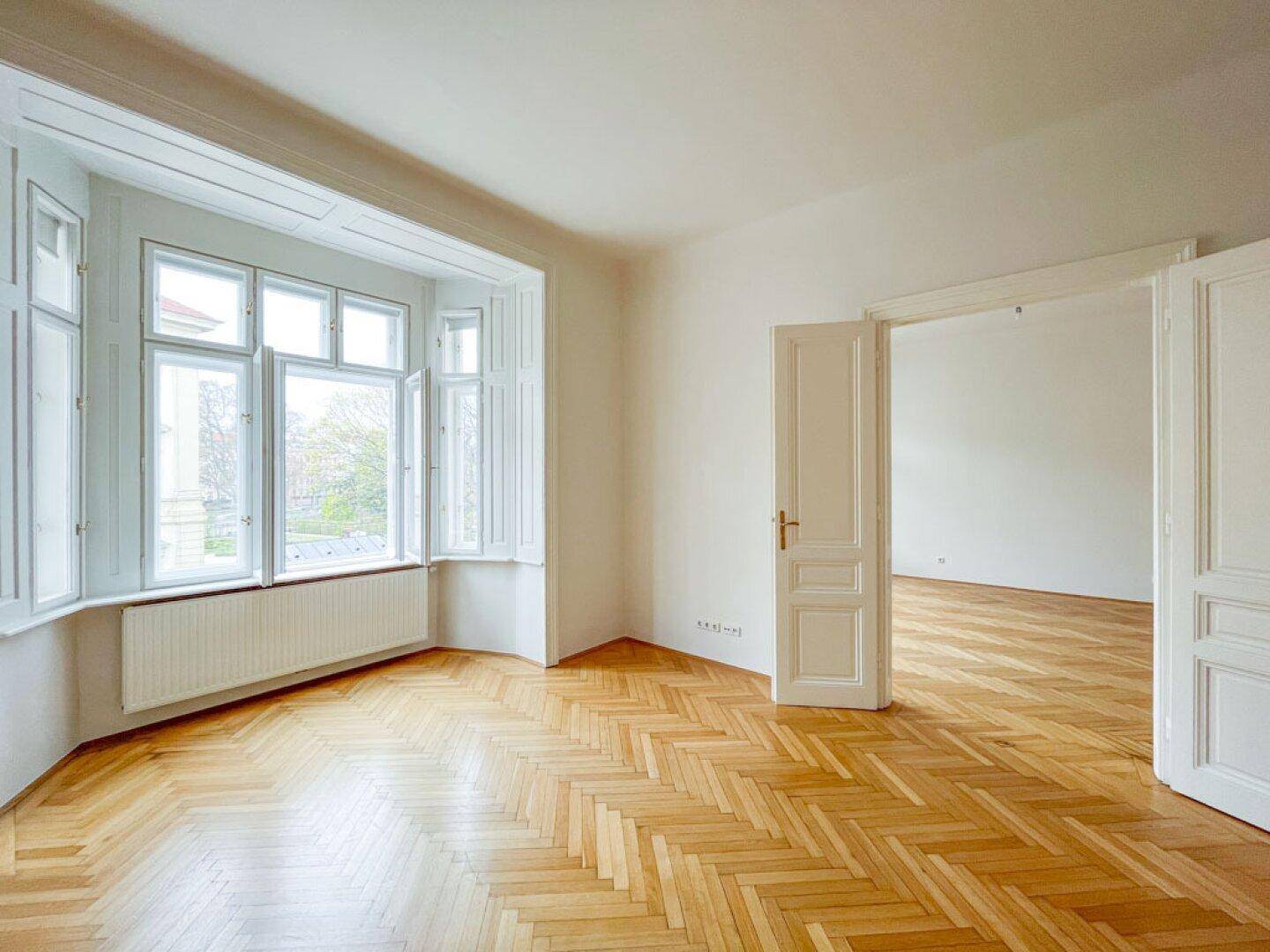 Geräumiges Zimmer mit klassischem Fischgrätparkett und einem charmanten Erkerfenster mit Fensterläden.