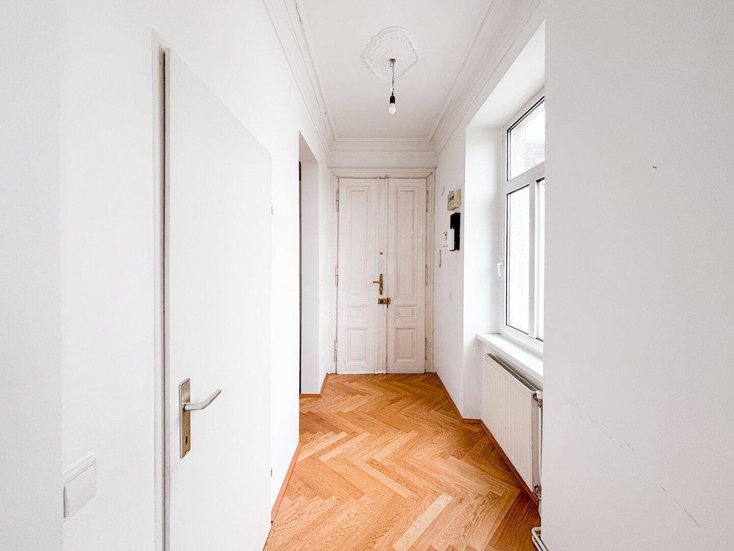 Eingangsbereich mit Fischgrätparkett, hohen Decken und einer Doppeltür zum Treppenhaus.