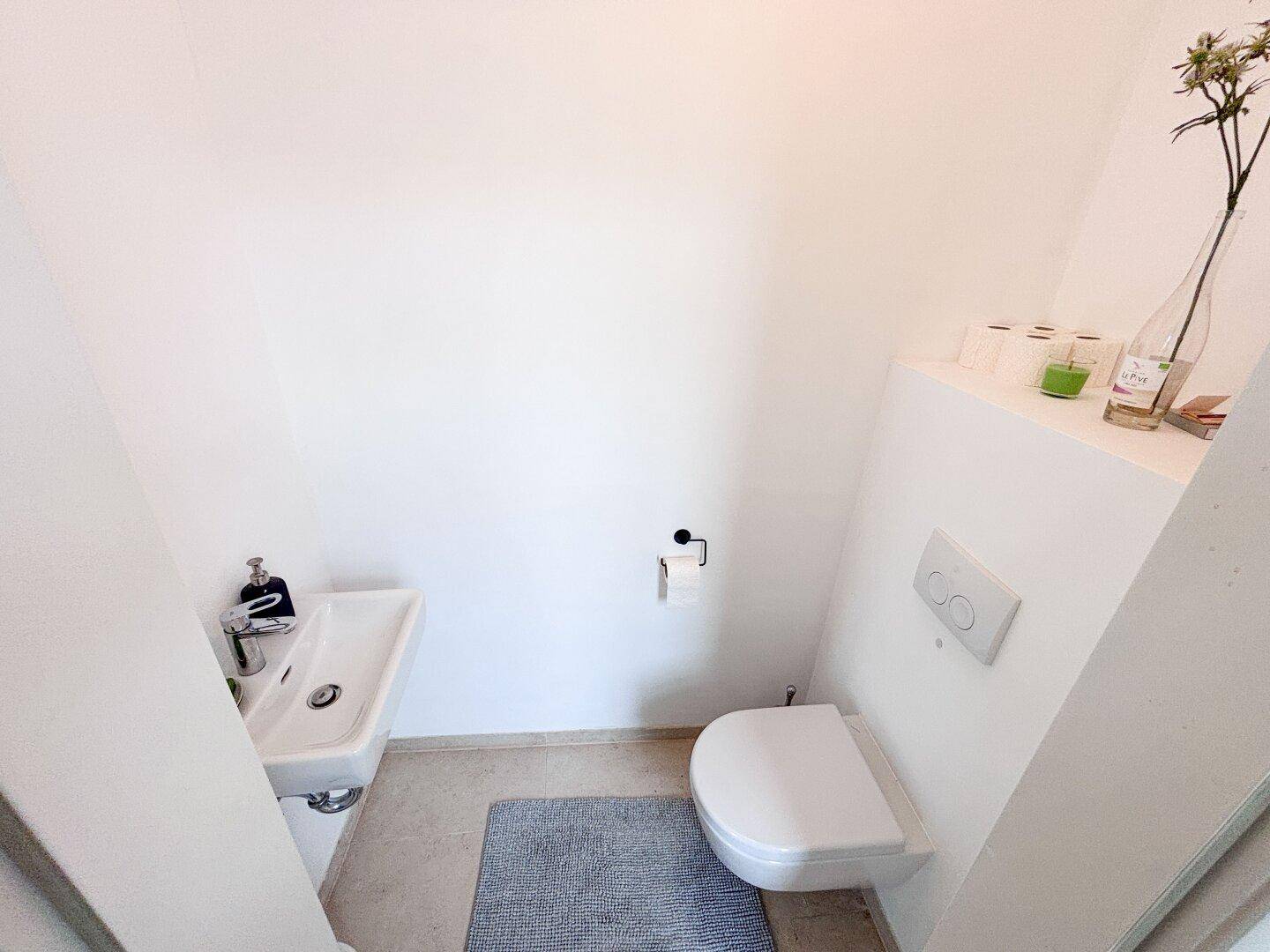 Kleines Gäste-WC mit wandhängendem WC und Waschbecken, minimalistisch gestaltet.