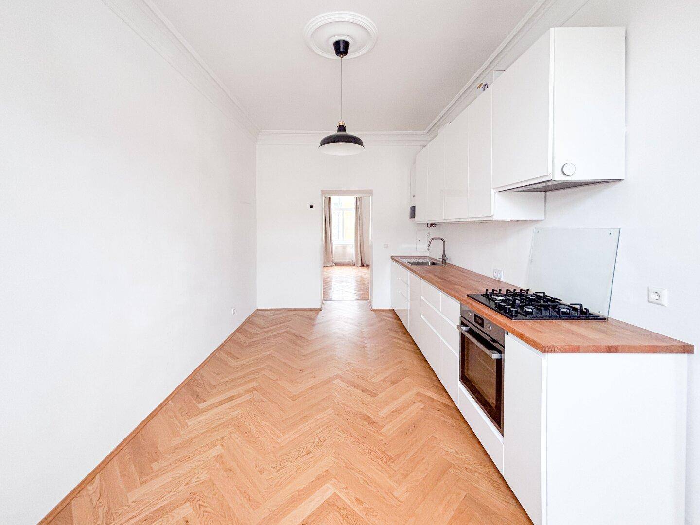 Schmale, moderne Küche mit weißen Schränken und Holz-Arbeitsplatte, offen zum Flur.