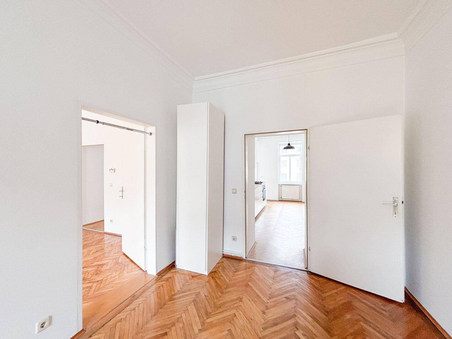 Geräumiger Flur mit Fischgrätparkett und integriertem Schrank, der zu weiteren Räumen führt.