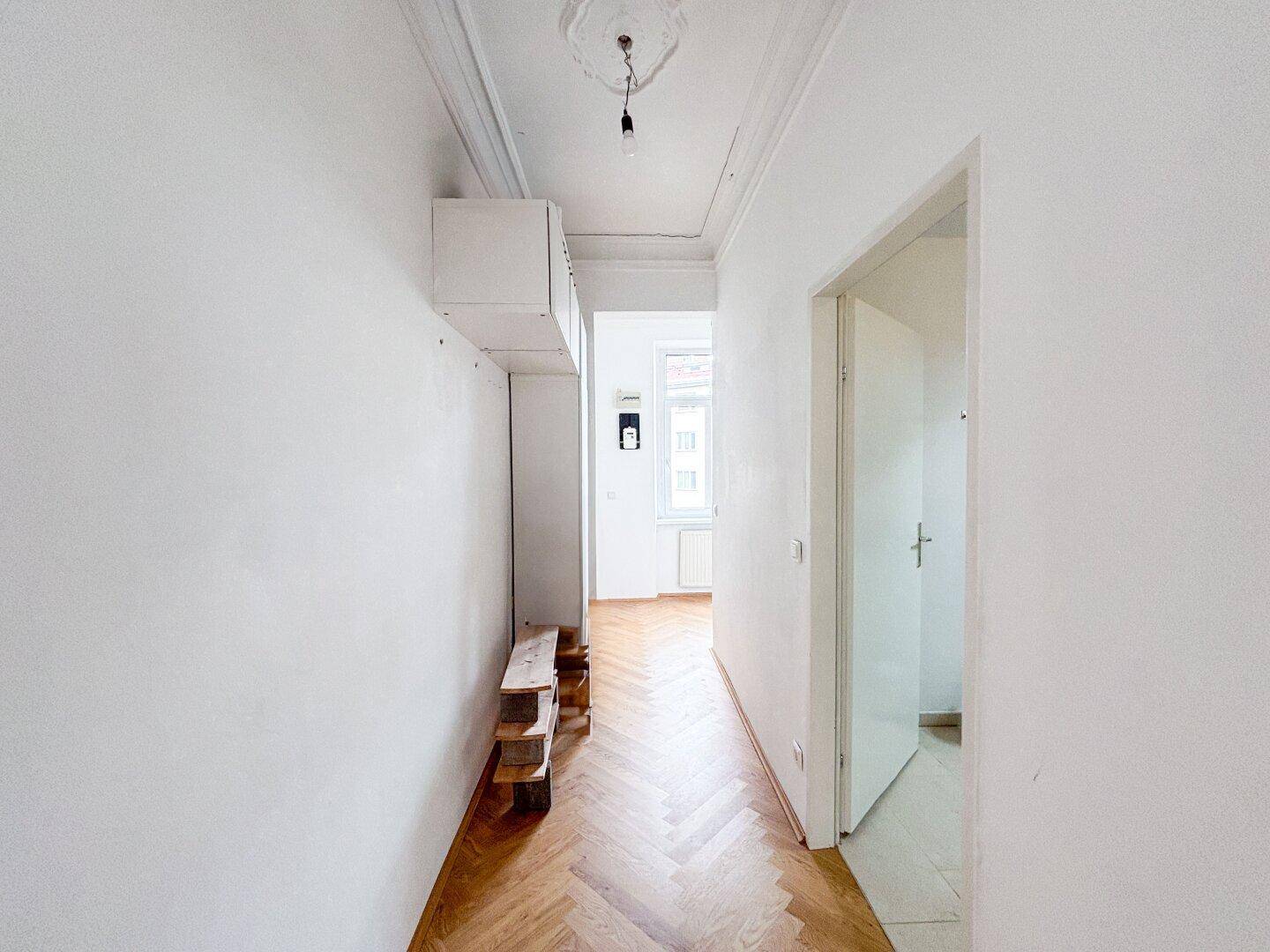Flur mit Fischgrätparkett und eingebauten Regalen, der zu den Zimmern der Wohnung führt.