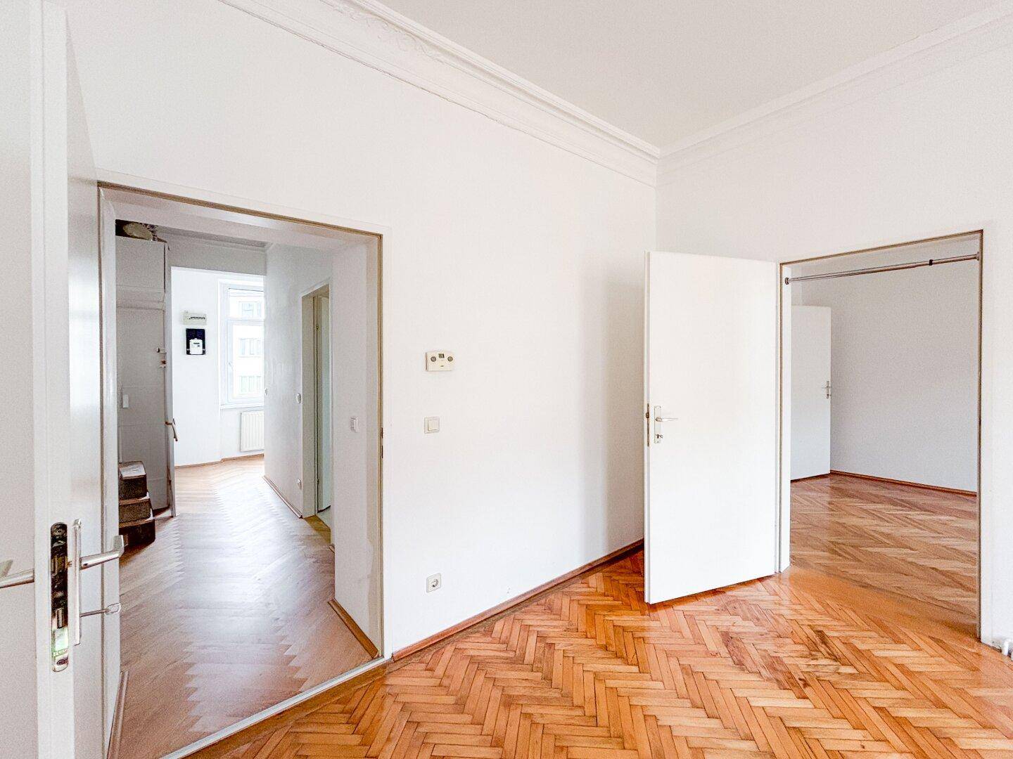 Heller Flur mit Fischgrätparkett, der verschiedene Räume der Wohnung miteinander verbindet.