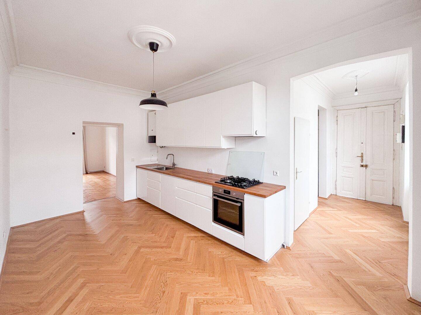 Moderne Einbauküche mit weißen Schränken, Holz-Arbeitsplatte und Gasherd, offen zum Wohnbereich.