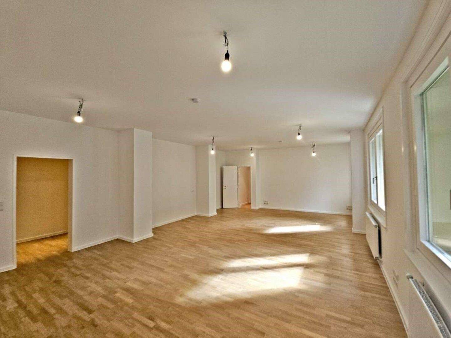 Geräumiger, heller Wohnbereich mit Parkettboden und mehreren Fenstern für viel Tageslicht.