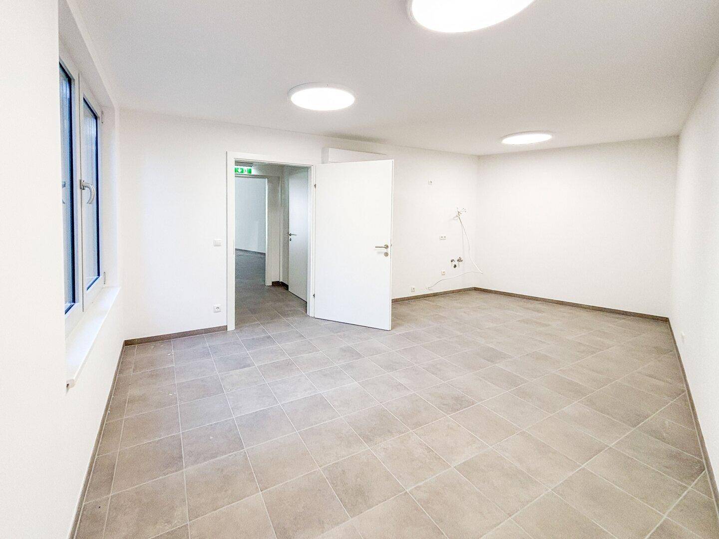 Geräumiger, leerer Gewerberaum mit Fliesenboden und Zugang zu weiteren Räumen, ideal für flexible Nutzung.