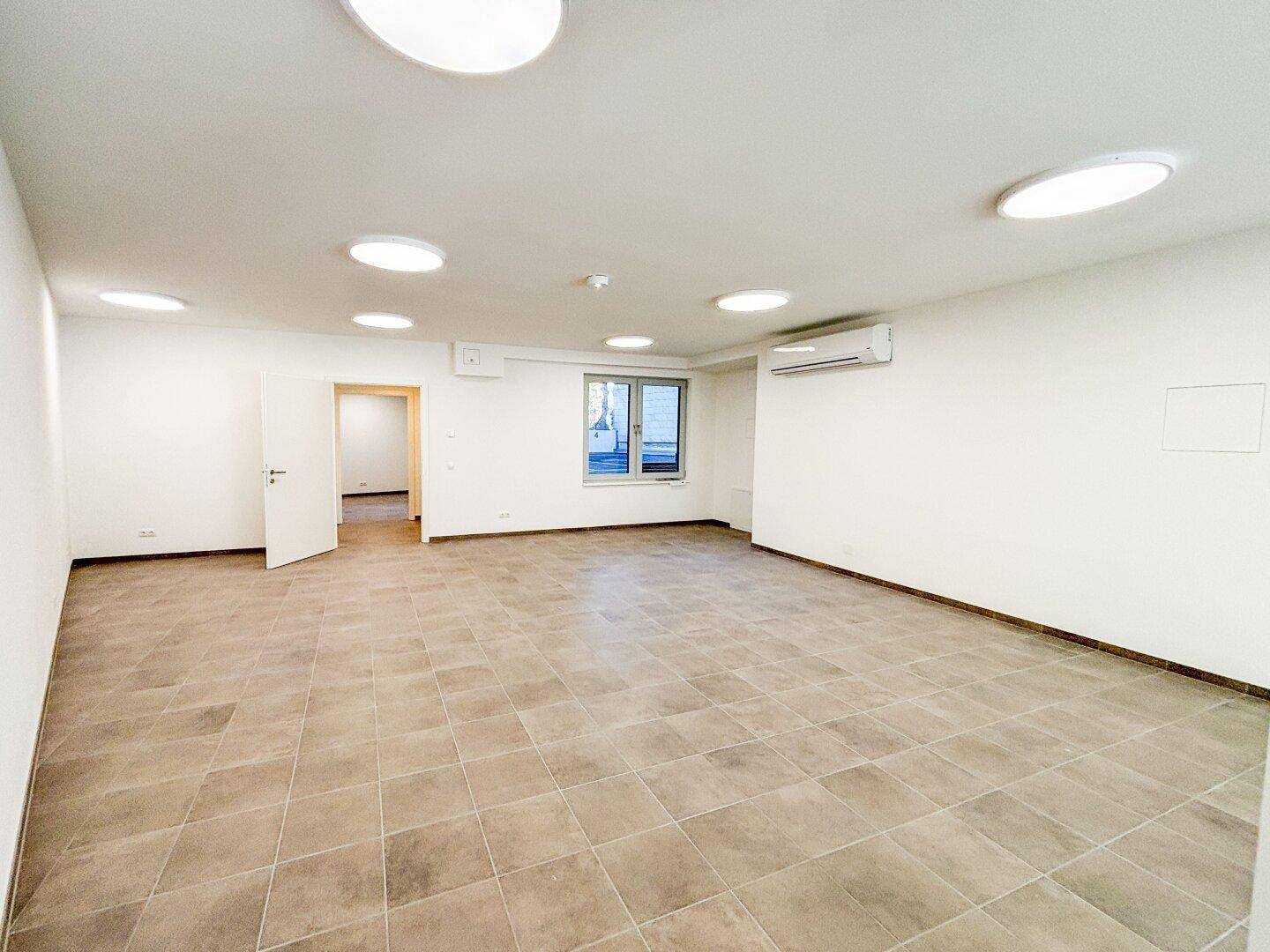 Großer, leerer Gewerberaum mit Fliesenboden, Fenster und Klimaanlage, bietet viel Platz für Geschäftsideen.