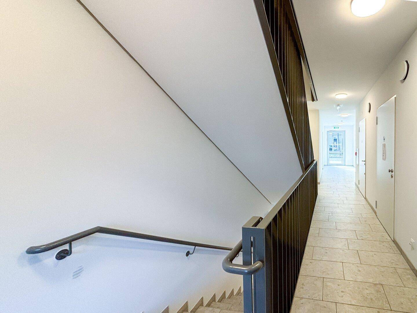 Modernes Treppenhaus mit Handlauf und Fliesenboden, das die Etagen des Gebäudes verbindet.