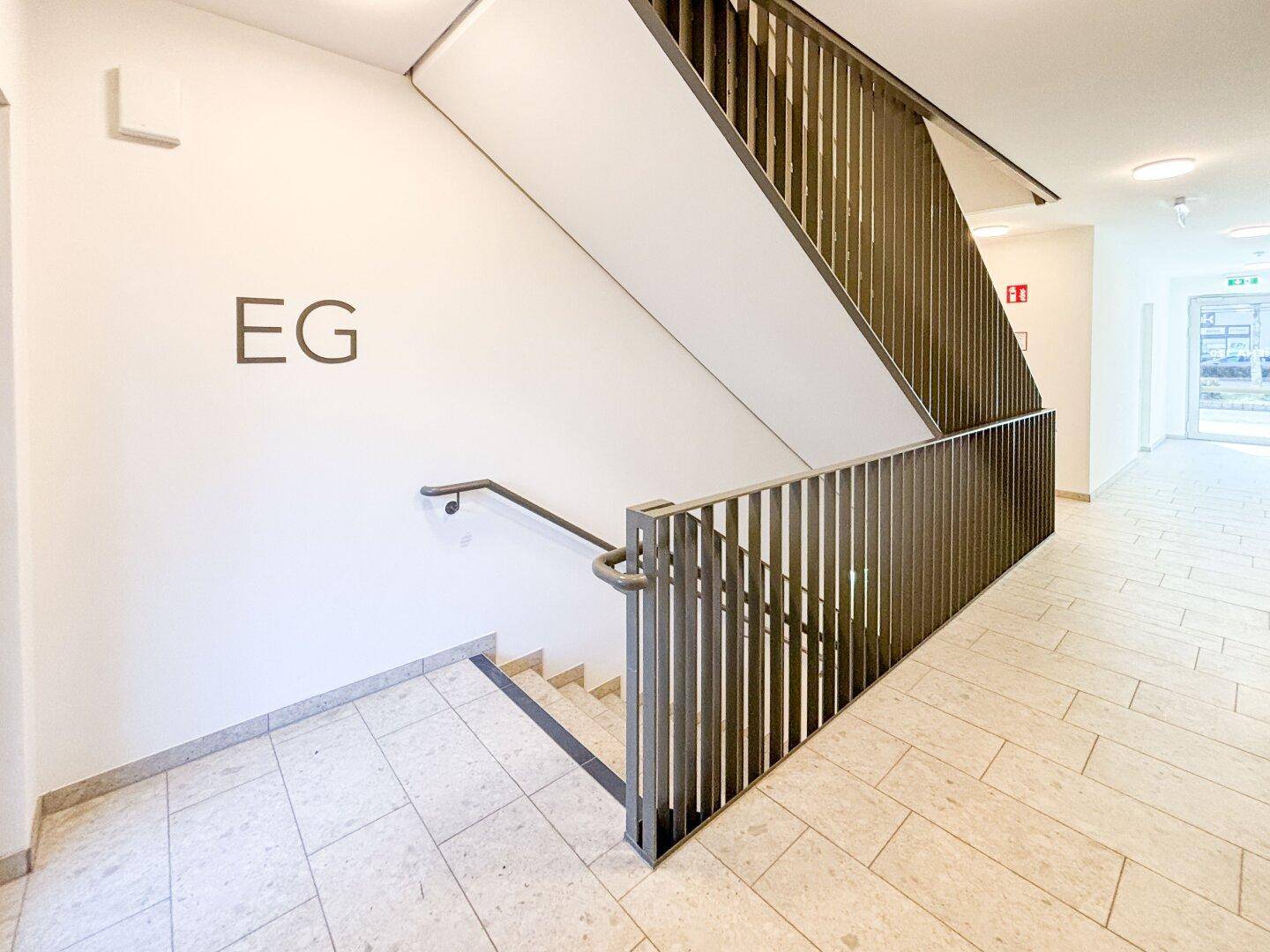 Treppenhaus mit Metallgeländer und Fliesenboden, das den Zugang zum Erdgeschoss ermöglicht.