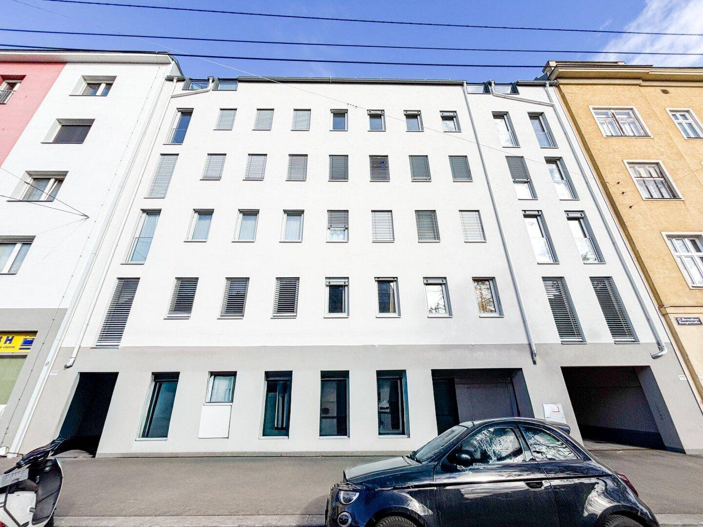 Moderne Gebäudefassade mit vielen Fenstern und Jalousien, integriert in eine städtische Umgebung.