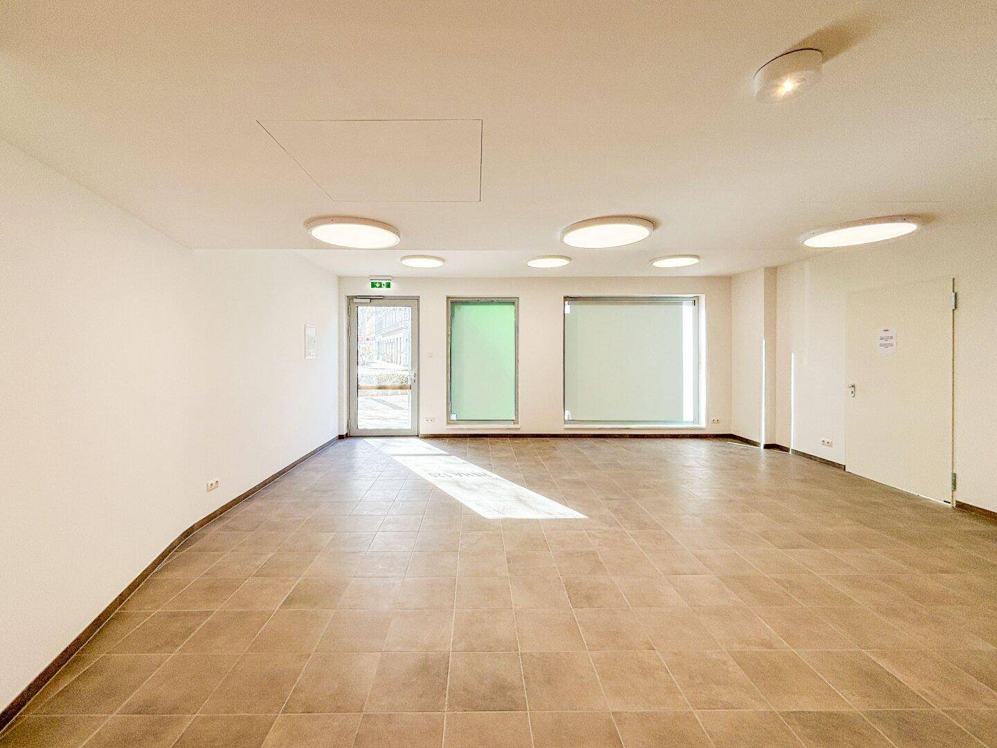 Leerer Gewerberaum mit großen Fenstern, Fliesenboden und Klimaanlage, bereit für die Erstnutzung.