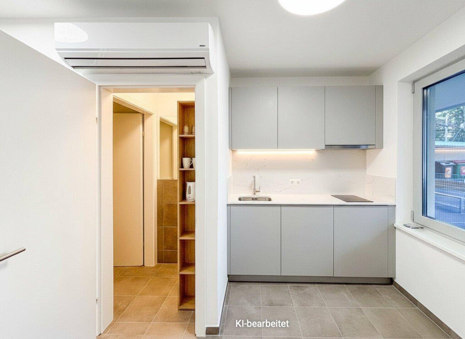 Moderne Küchenzeile mit grauen Schränken, Spüle und Kochfeld, ideal für kleine Büros oder Studios, mit Klimaanlage.