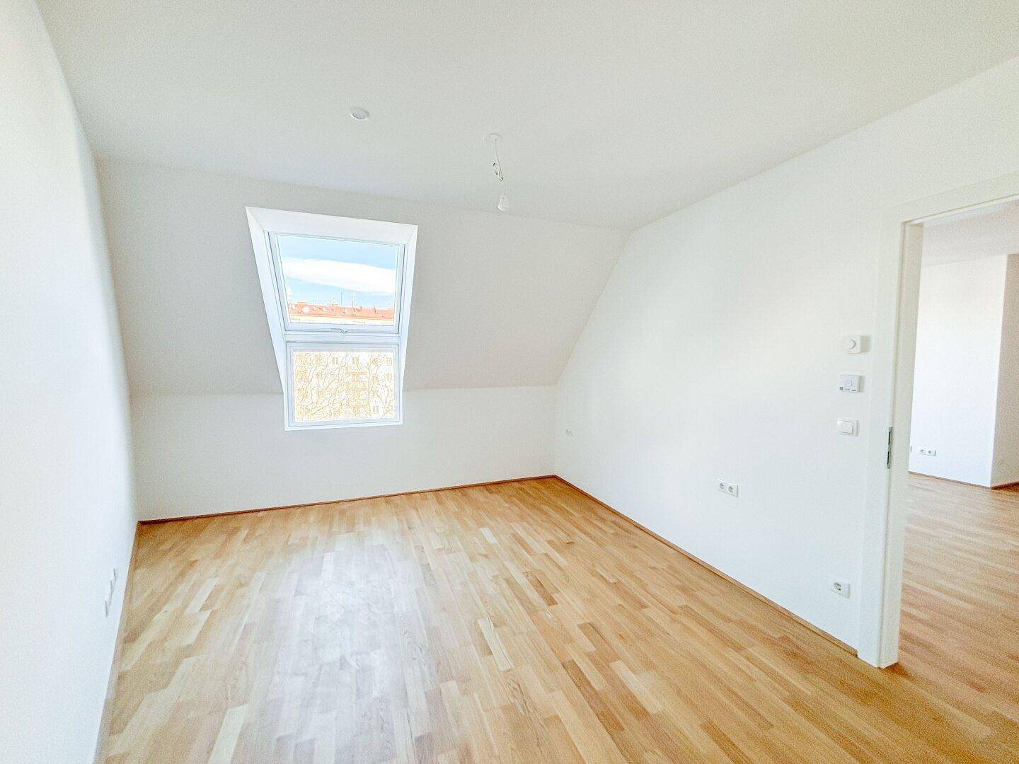 Helles Dachgeschosszimmer mit Holzboden und einem großen Dachfenster für viel Tageslicht.