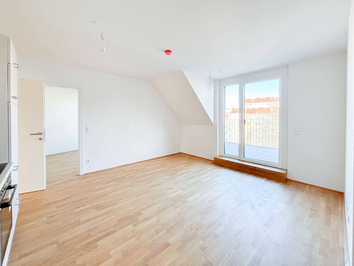 Lichtdurchfluteter Wohnbereich mit offener Küche, Holzboden und Zugang zu einem sonnigen Balkon.