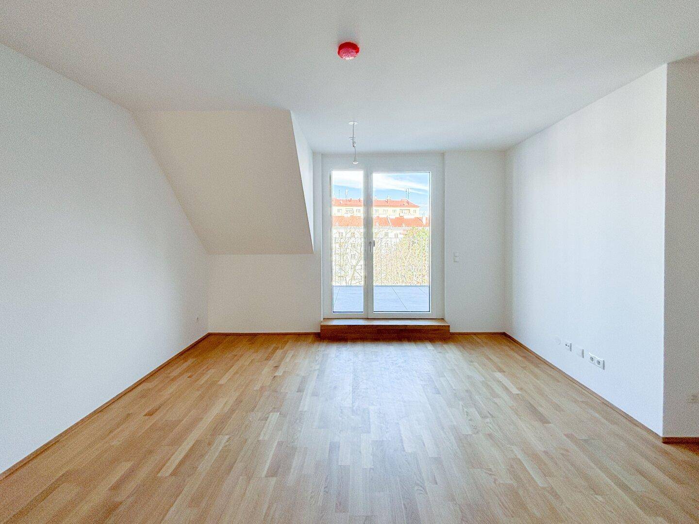 Geräumiger Raum mit Holzboden und Zugang zu einem Balkon, ideal als Wohn- oder Schlafzimmer.