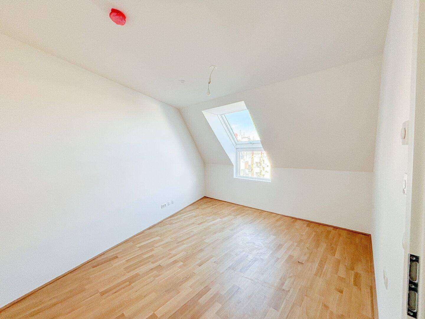 Dachgeschosszimmer mit Holzboden und schrägem Dach, ausgestattet mit einem hellen Dachfenster.