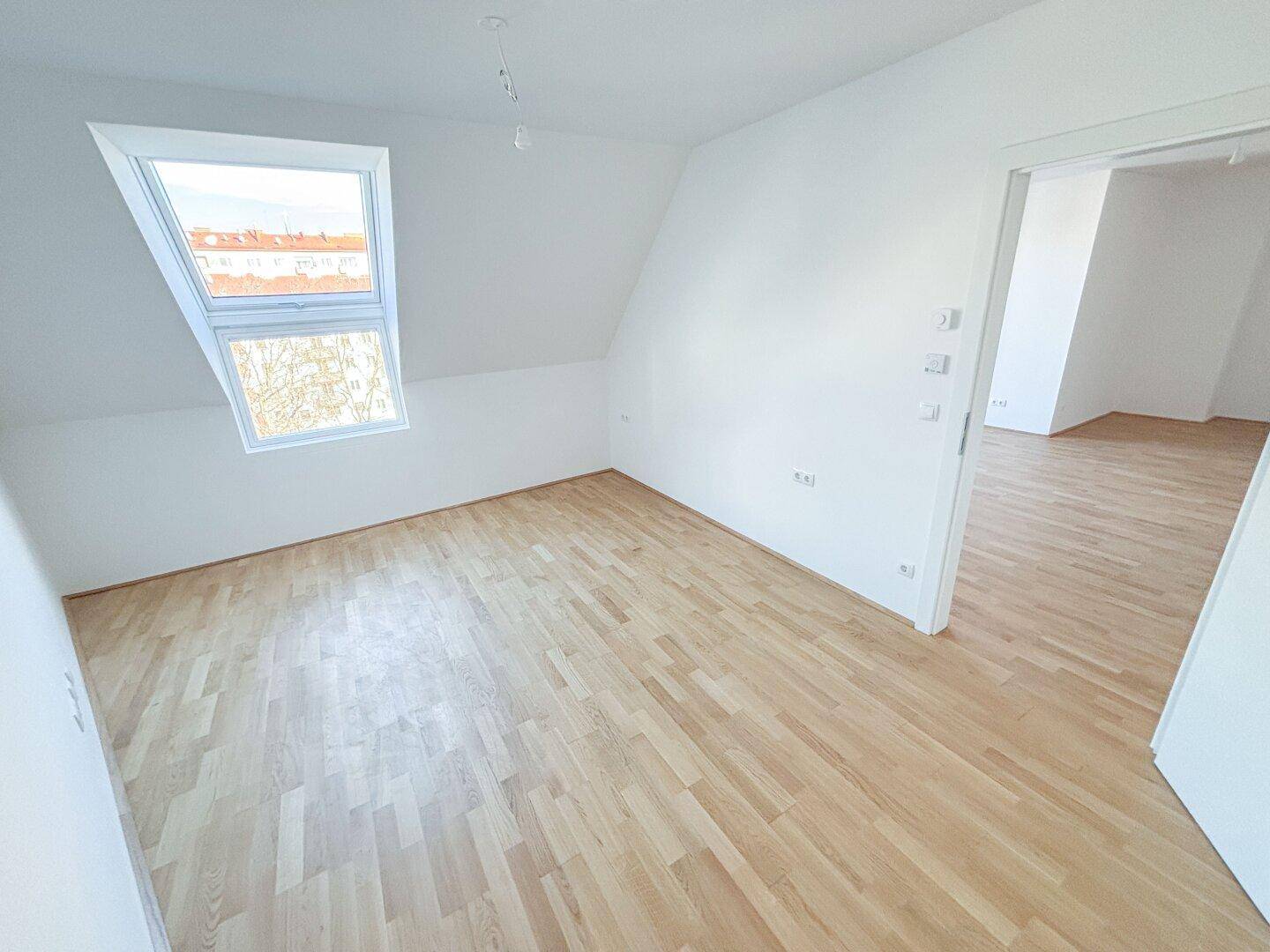 Helles Schlafzimmer im Dachgeschoss mit Holzboden und einem großen Dachfenster, bereit zur Einrichtung.