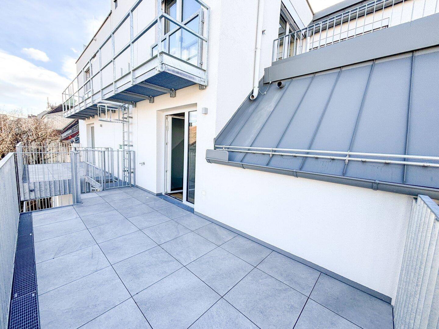 Geräumiger Balkon mit Fliesenboden und Metallgeländer, Teil eines modernen Neubaus.