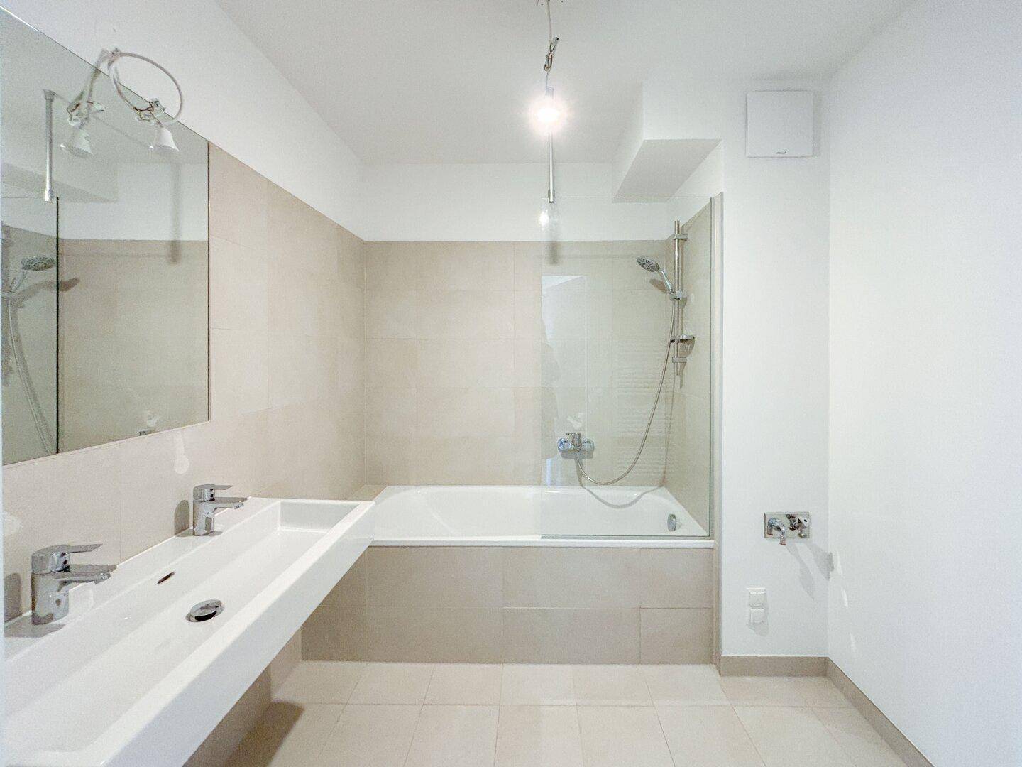 Modernes Badezimmer mit Badewanne, Dusche und Doppelwaschbecken, in hellen Farbtönen gehalten.