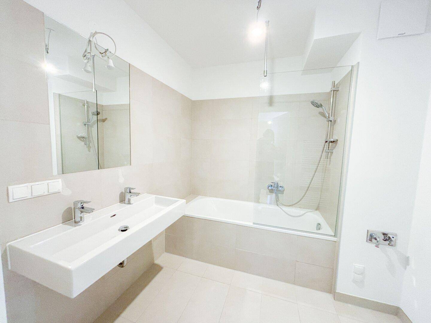 Helles Badezimmer mit Badewanne, Dusche und Doppelwaschbecken, modern gefliest.