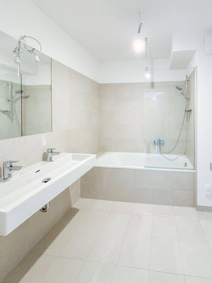 Zeitgemäßes Badezimmer mit Badewanne, Dusche und Doppelwaschbecken, mit neutralen Fliesen.