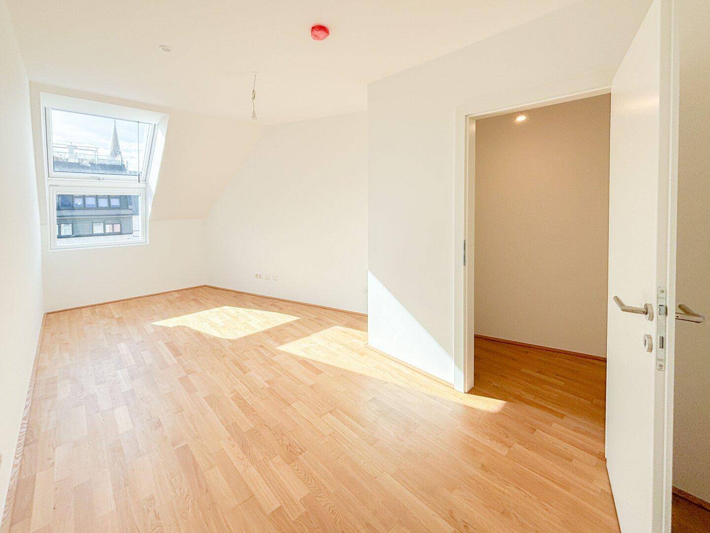 Geräumiges Dachgeschosszimmer mit Holzboden und Dachfenster, bietet viel natürliches Licht.