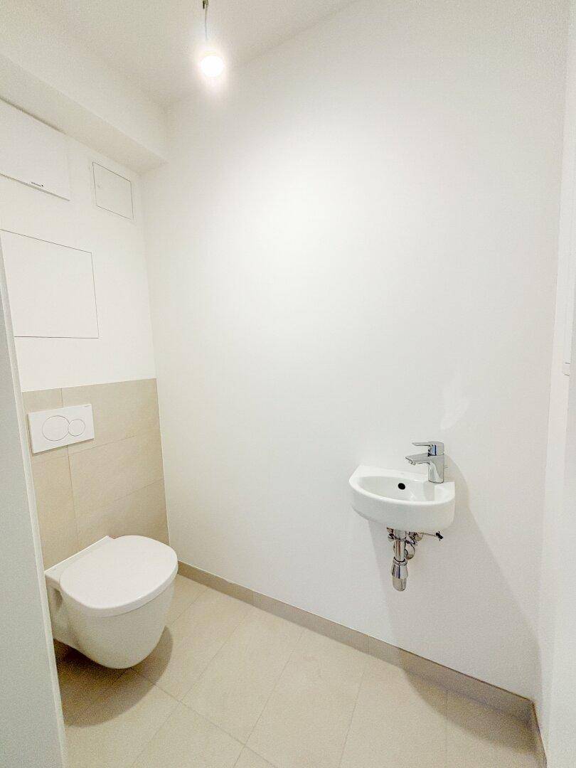 Modernes Gäste-WC mit wandhängender Toilette und kleinem Waschbecken, in neutralen Farben.